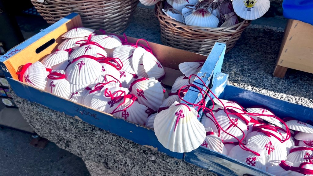A wooden crate filled with white scallop shells tied with red ribbons, displayed alongside a woven basket of additional shells.