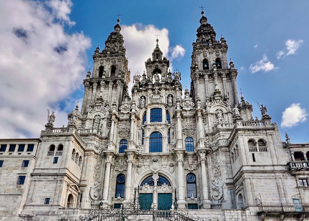 Front view of a grand, ornate cathedral with multiple spires and detailed sculptures against a blue sky with clouds.