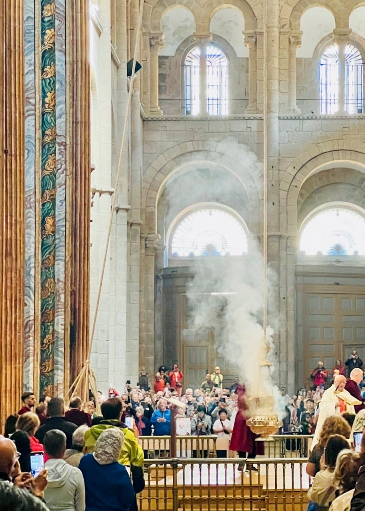 Interior of a grand church filled with people, observing a religious ceremony involving a swinging thurible emitting smoke.